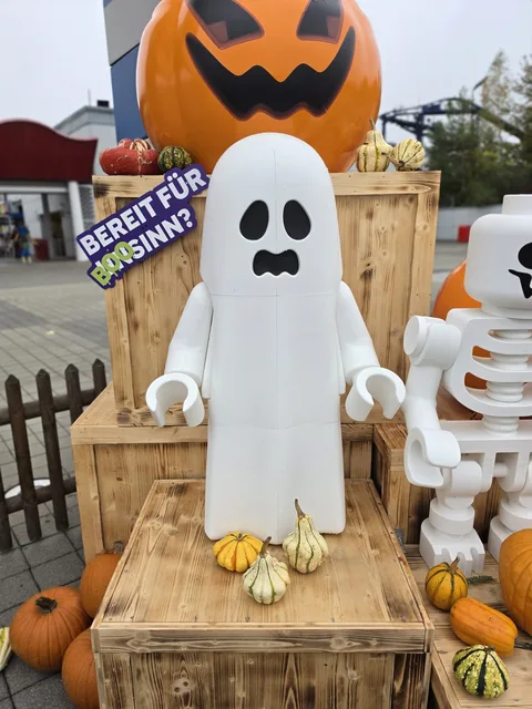 Ein aus Steinen gebautes Gespenst als Minifigur, größer als ein Kind, vor einem riesigen geschnitzten Kürbis, daneben ein Schild „Bereit für BOOsinn?“