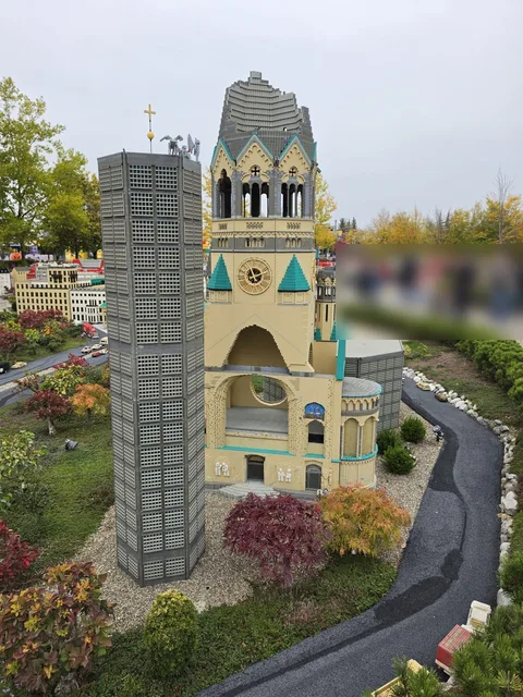 Die Kaiser-Wilhelm-Gedächtniskirche im Miniland: der zerstörte alte Turm mit der abgebrochenen Spitze neben dem neuen achteckigen Glockenturm, ringsum rote und orange Sträucher