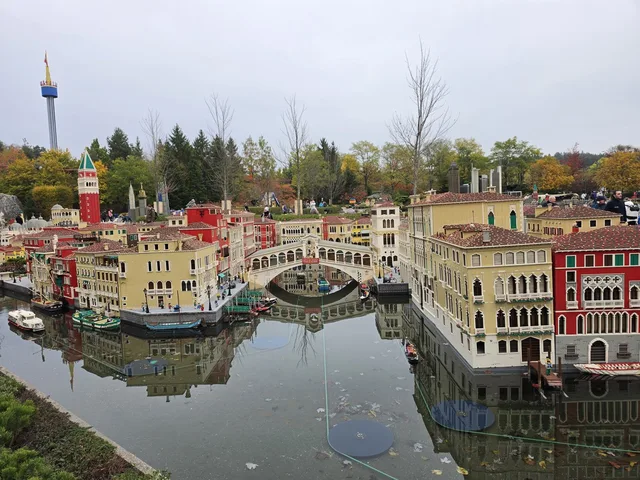 Venedig im Miniland: die Rialtobrücke über einem Kanal mit roten und ockerfarbenen Palazzi, gespiegelt im ruhigen Wasser, im Hintergrund der Campanile