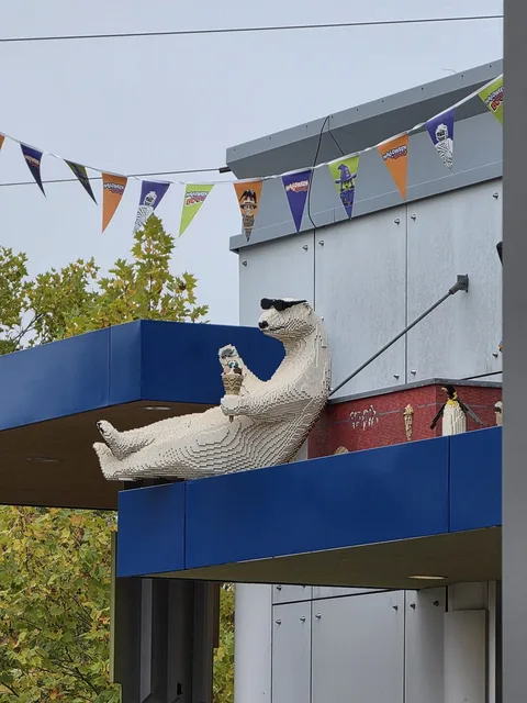 Ein großer Eisbär aus Steinen mit Sonnenbrille, zurückgelehnt auf einer blauen Dachkante, eine Eistüte in der Pfote, darüber Halloween-Wimpel, daneben ein Pinguin aus Steinen