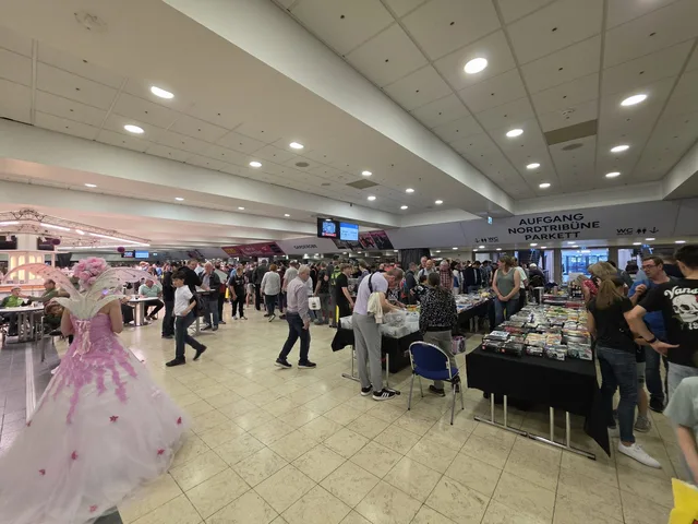 Das Foyer der Grugahalle während der Lego-Börse: Besucher an langen Tischen voller loser Minifiguren, im Vordergrund eine Cosplayerin in rosa-weißem Kleid