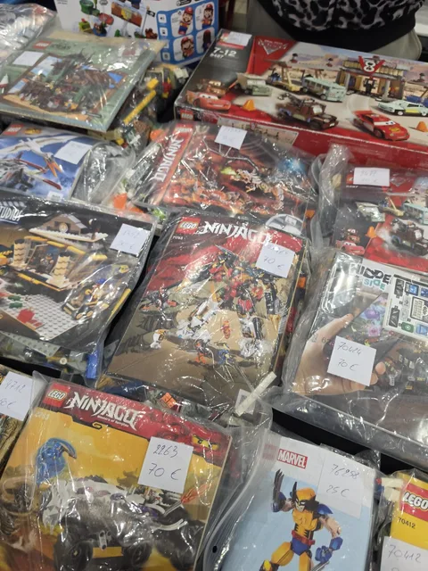 Gebrauchte LEGO-Sets in verschlossenen Beuteln auf einem Händlertisch, jeder mit einem handgeschriebenen Preisschild