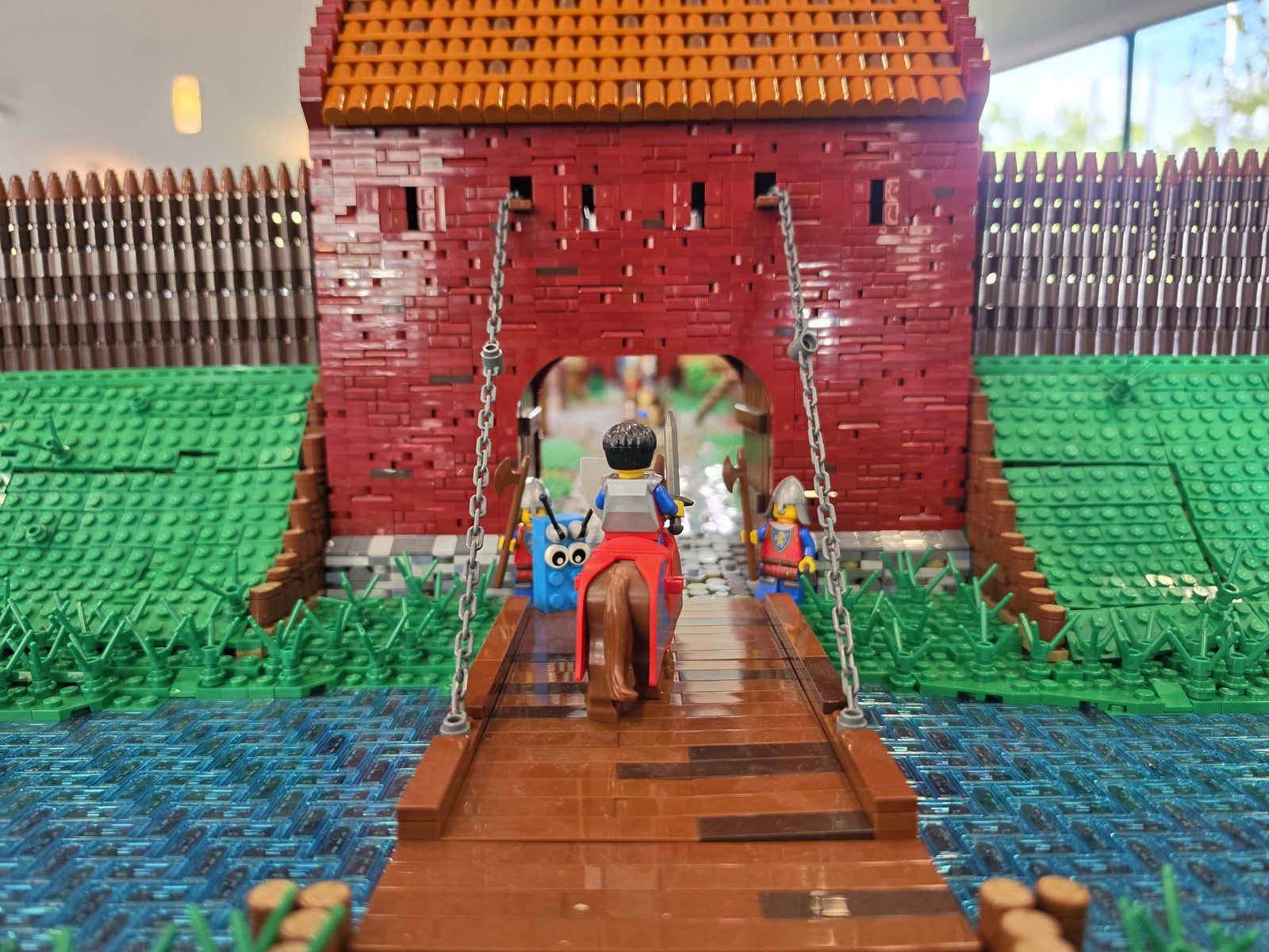Nahaufnahme eines roten Burgtors aus LEGO mit hölzerner Zugbrücke über einem Wassergraben