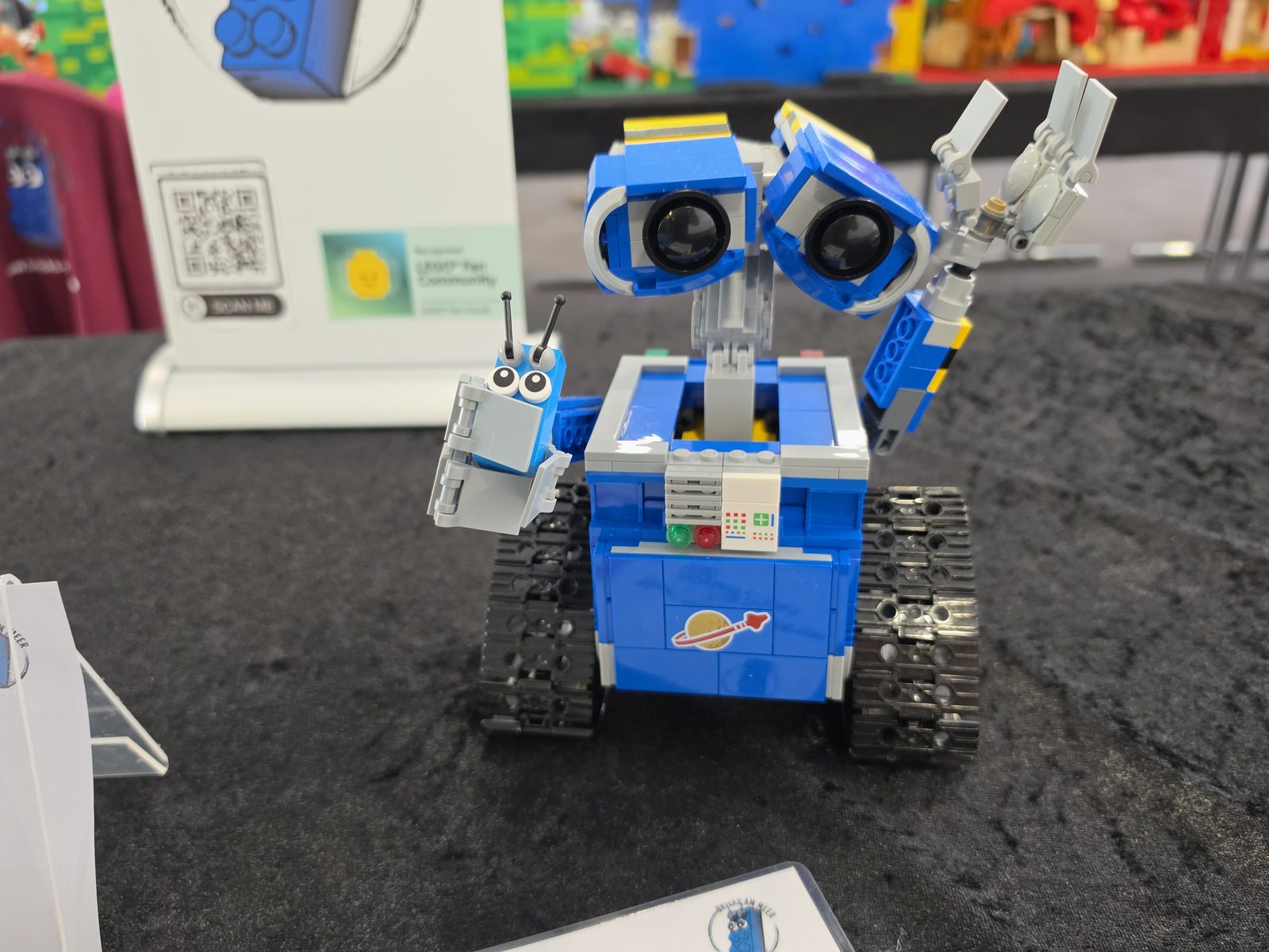 Ein blauer Roboter aus LEGO-Steinen mit großen Augen, daneben das Maskottchen von Bricks am Meer
